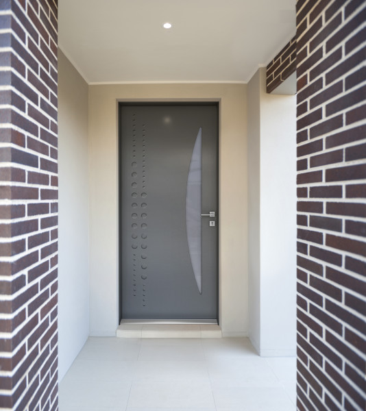 Porte d'entrée acier BONO - Visuel d'ambiance Entrée vue de l'extérieur avec porte d'entrée grise composée d'une surface vitrée et d'un décor